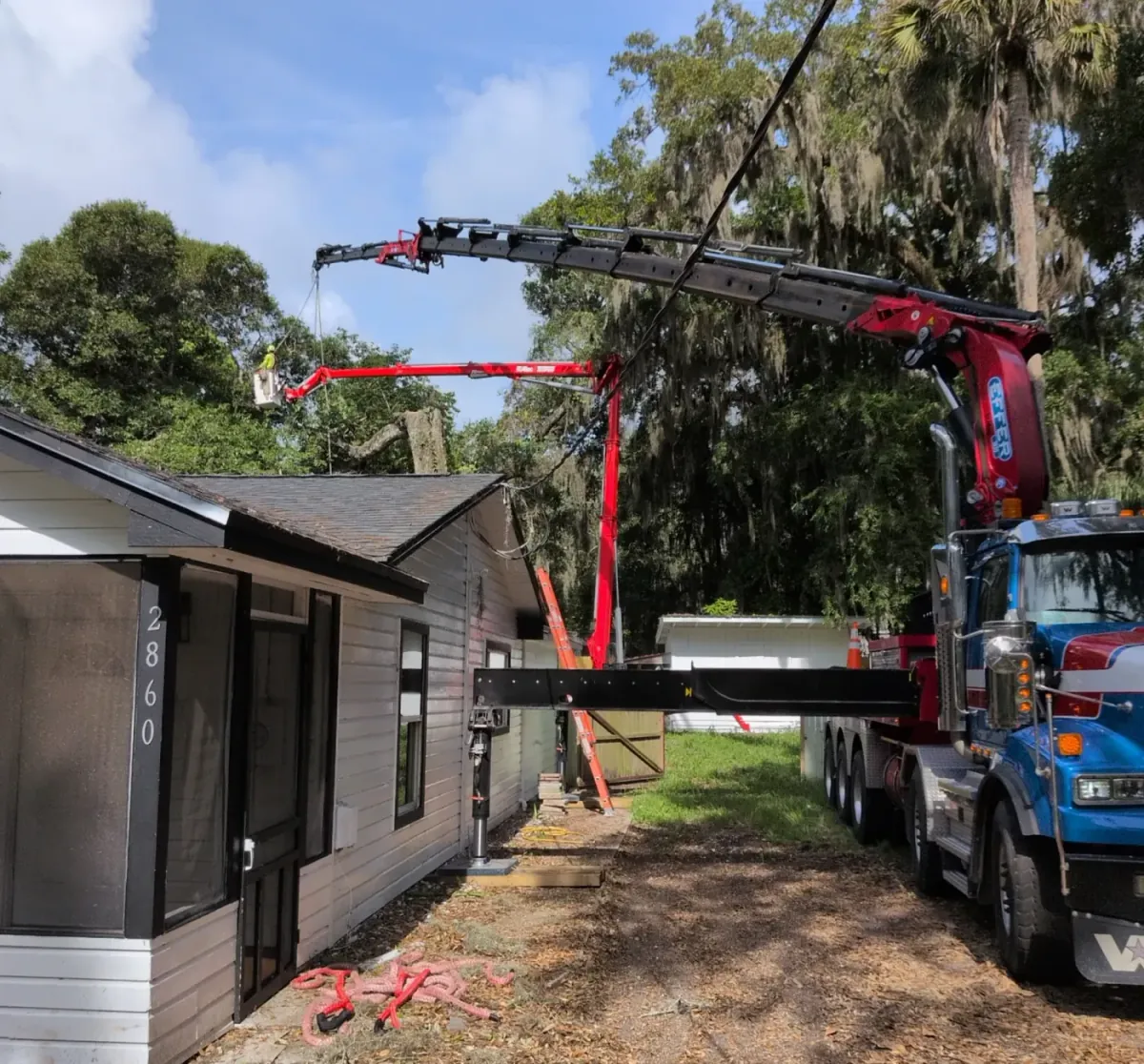 Jax Tree Removal blue crane truck and aerial lift working a moss-draped oak alongside a single-story home in Jacksonville, FL