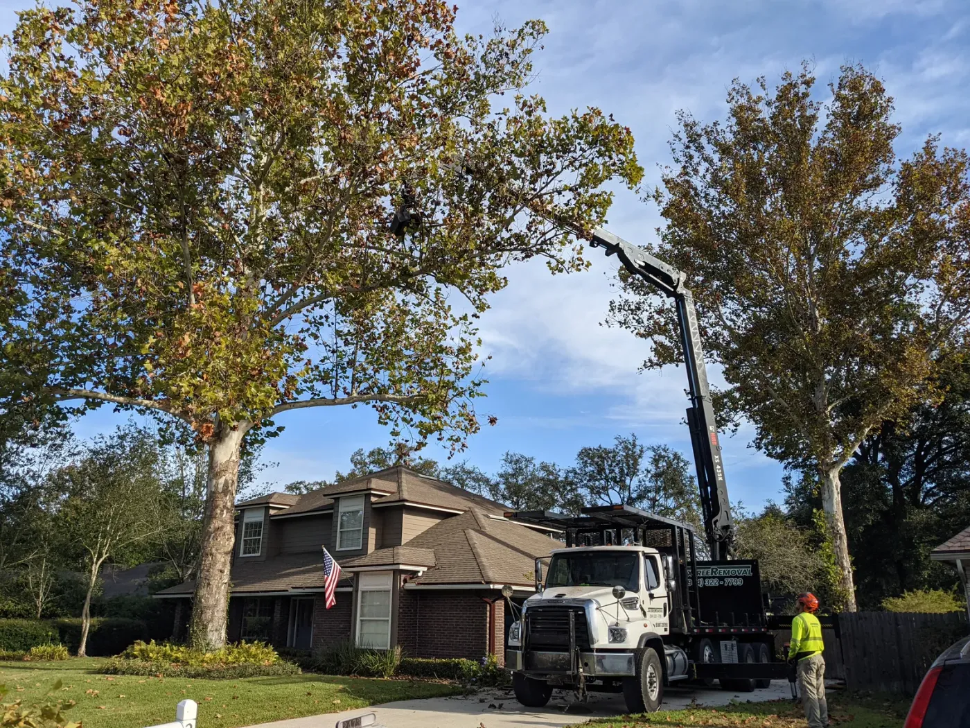Knuckle-boom crane reaching over a two-story brick home — crane tree removal in Jacksonville, FL by Jax Tree Removal